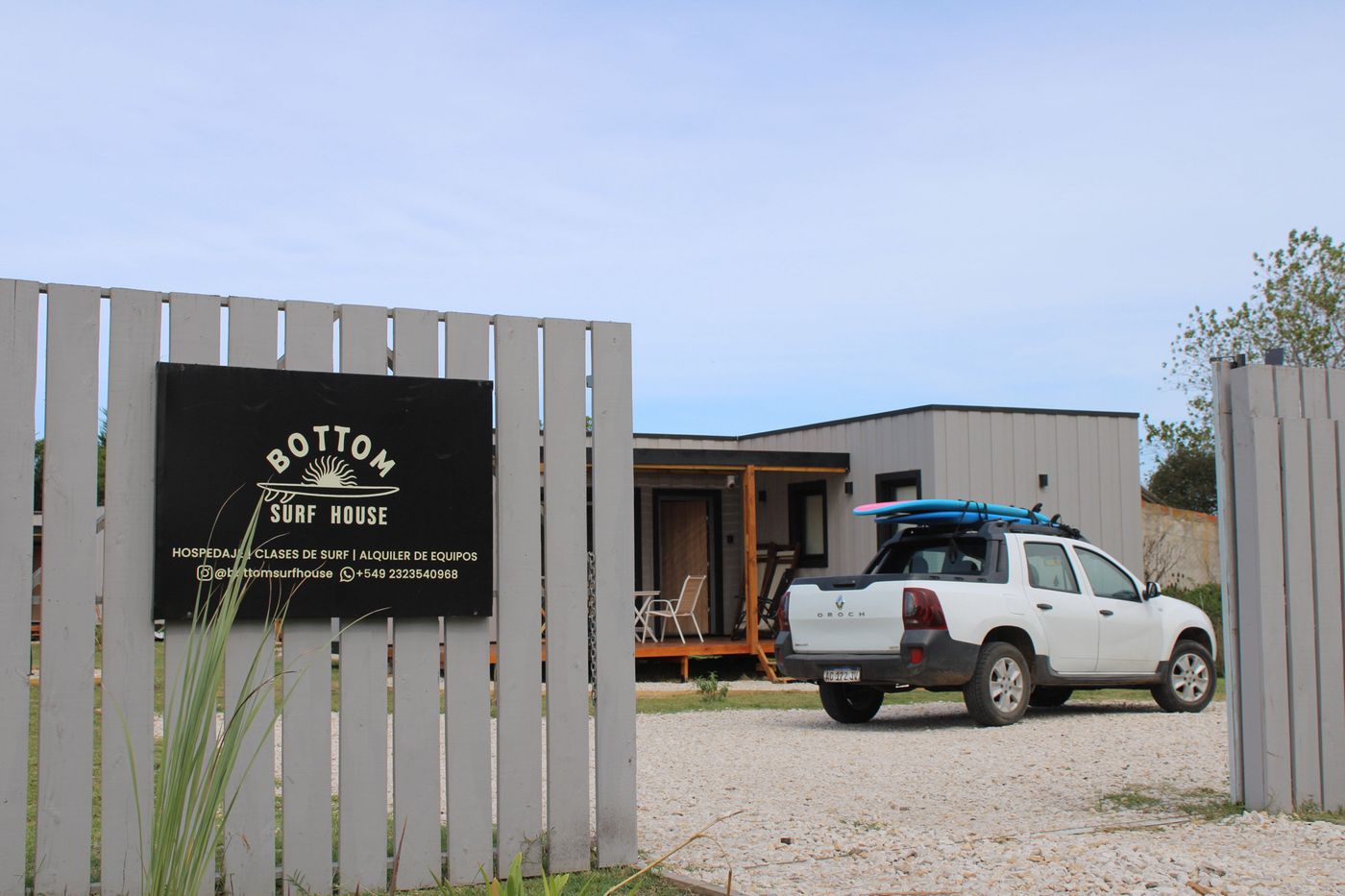 El cartel de Bottom Surf House en la entrada, con una camioneta con tablas