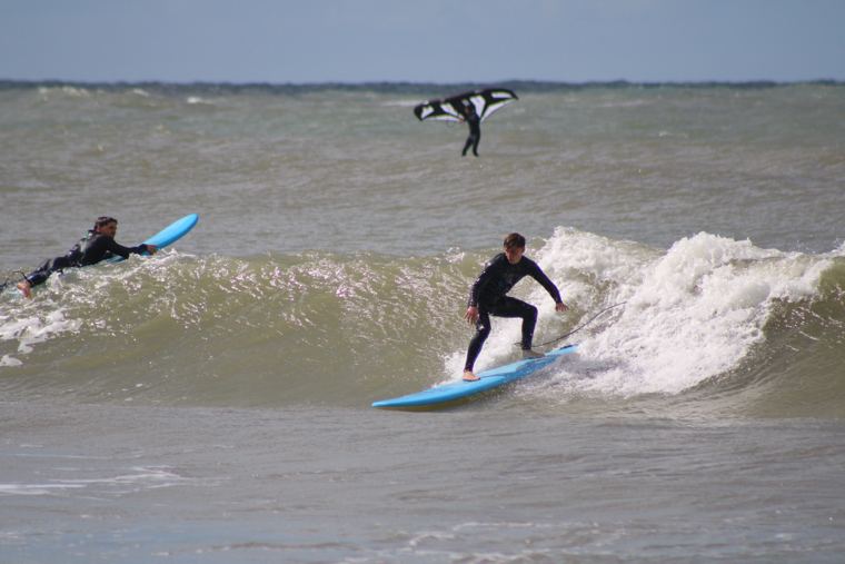 Alumno surfeando mientras otro rema al lado